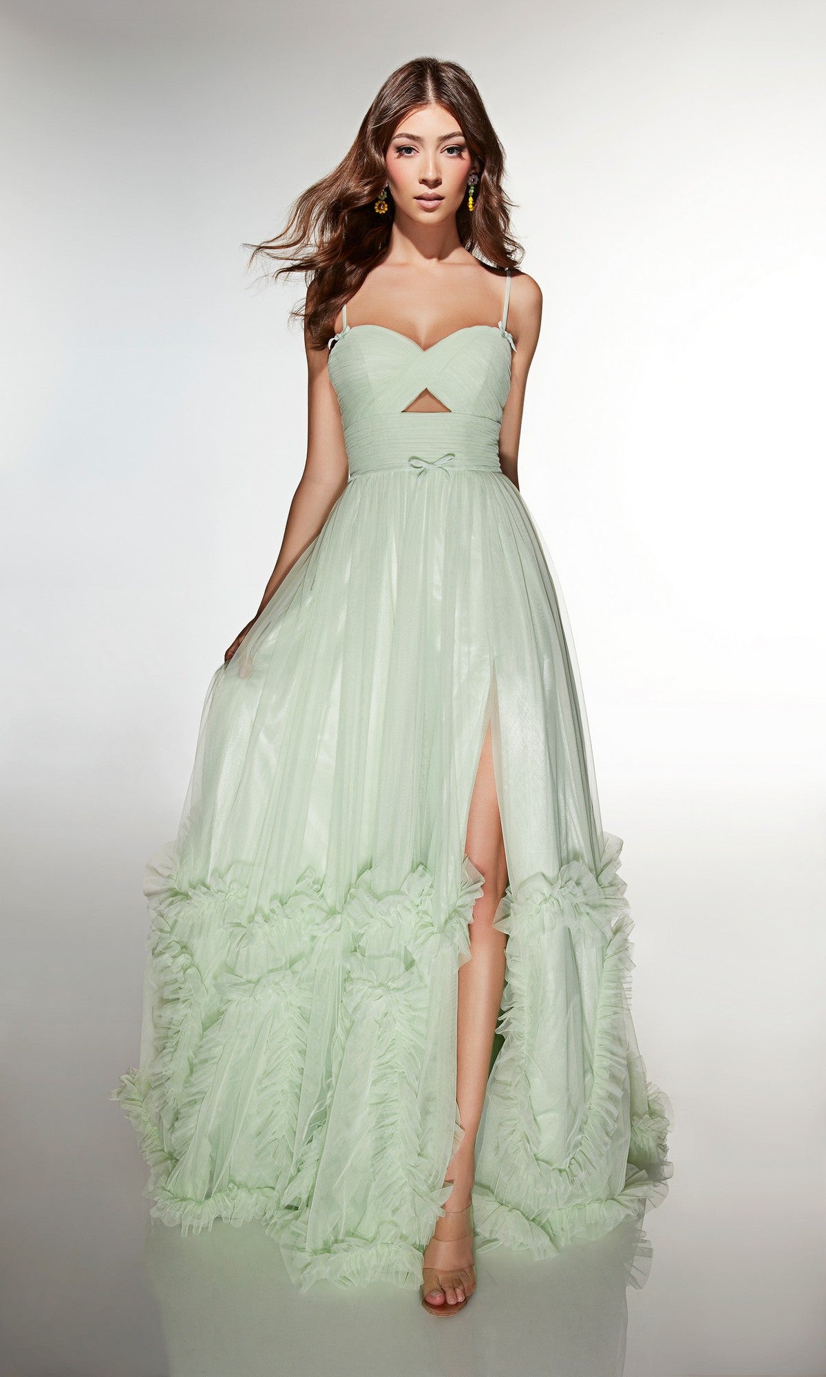 A woman models the Alyce 62043 long prom dress, featuring pale green color, sleeveless design, spaghetti straps, ruffled layers, and a thigh-high slit against a plain light background.